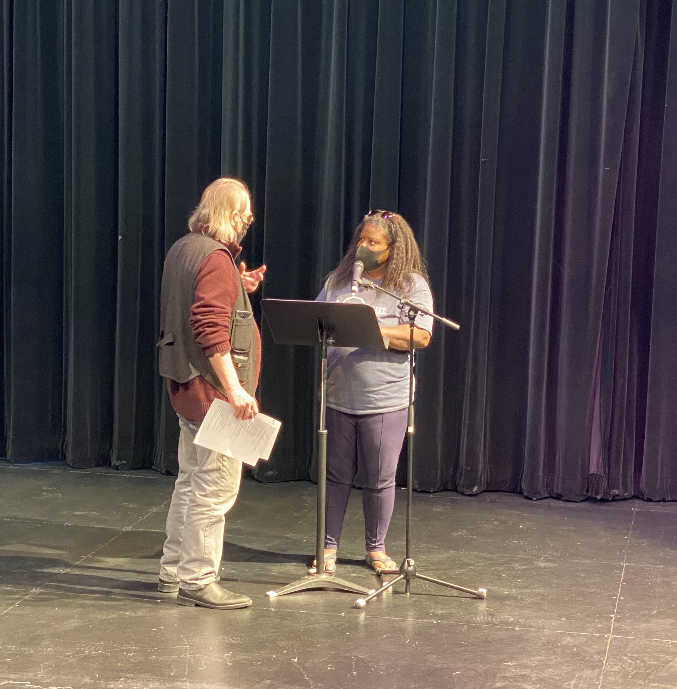 Artistic Director Kim Allen Bent stands (with pages of poem in his hand) with actor Shanda Williams (at music stand & mic) on stage at LNT, providing text analysis to Shanda